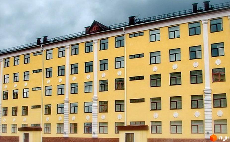 Зовнішній вигляд жовтої новобудови з численними вікнами. Будинок має кілька поверхів та сучасний дизайн фасаду.