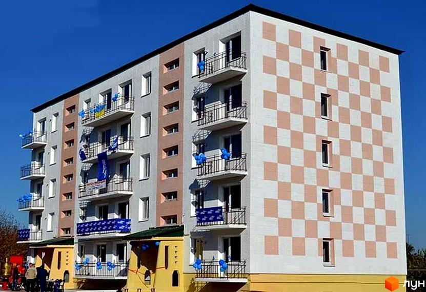 Новобудова на пров. Фестивальний, 3а, з фасадом у шаховому візерунку та балконами, прикрашеними синіми та жовтими кульками. Навколо будівлі видно елементи прибудинкової території.