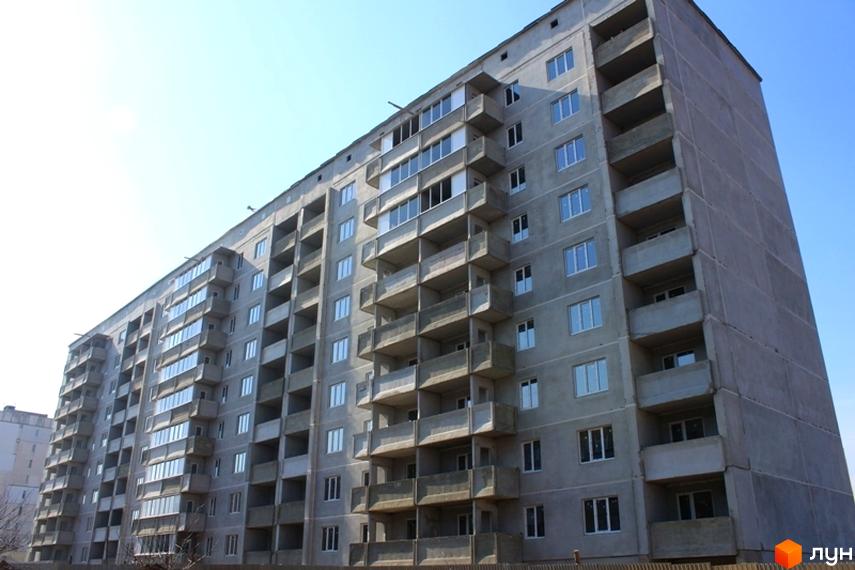 Зовнішній вигляд новобудови на вул. Башкірцевої, 33, корп. 2. Бетонний фасад, балкони та вікна будівлі на тлі блакитного неба.