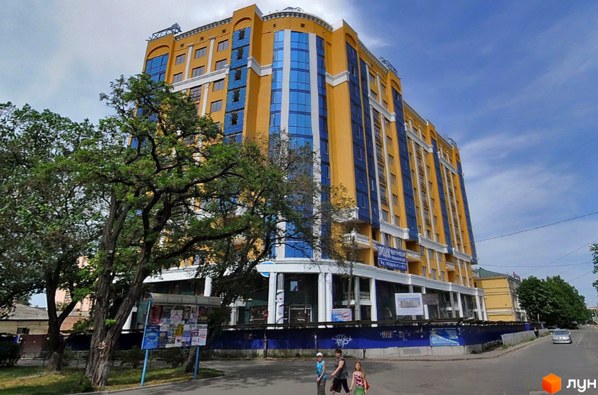 Житловий комплекс на вулиці Івана Банка (Коваля), 2 – жовто-блакитна багатоповерхова новобудова з великими вікнами. Поруч дерева та міська вулиця.