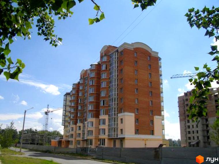Житловий комплекс на вул. Олександра Бідного, 16, з теракотовим фасадом та панорамними вікнами. Навколо видно зелені дерева та будівельні крани.