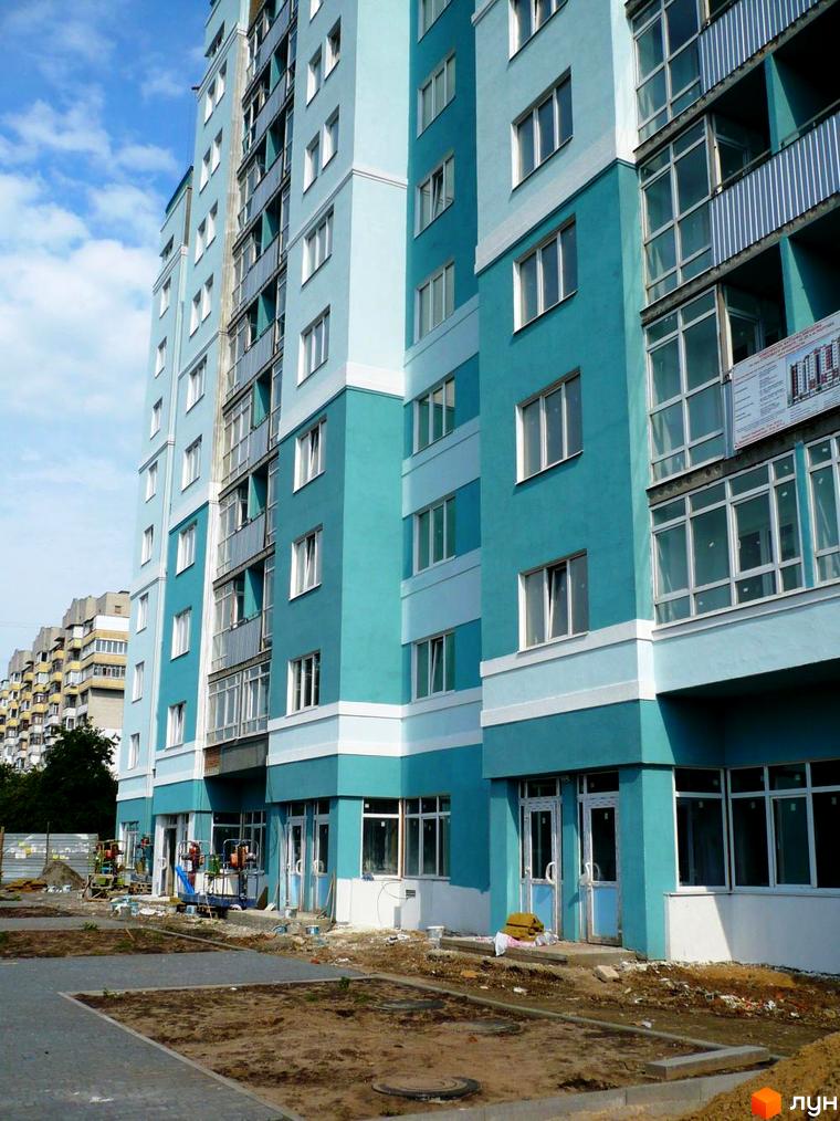 Новобудова на вул. Олександра Оксанченка, 18-28, з фасадом бірюзового та світло-блакитного кольорів, вікнами та заскленими балконами. Прибудинкова територія на етапі благоустрою.
