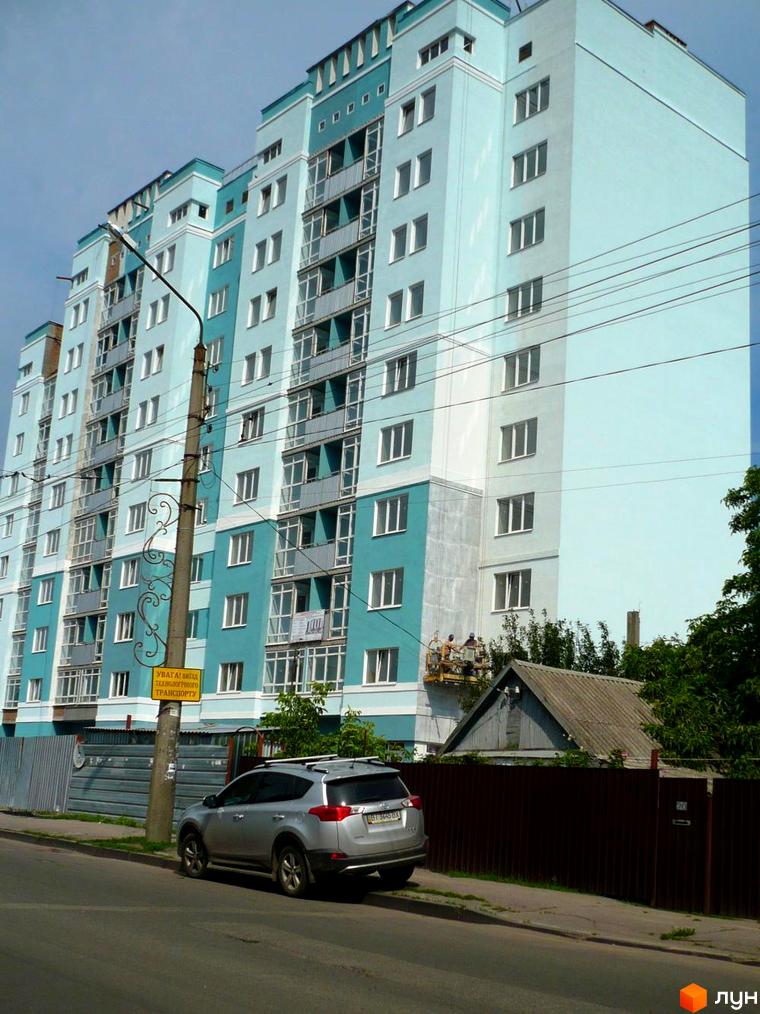 Житловий комплекс світло-блакитного кольору на вул. Олександра Оксанченка (Степового Фронту), 18-28. На передньому плані припаркований автомобіль та вуличний стовп.