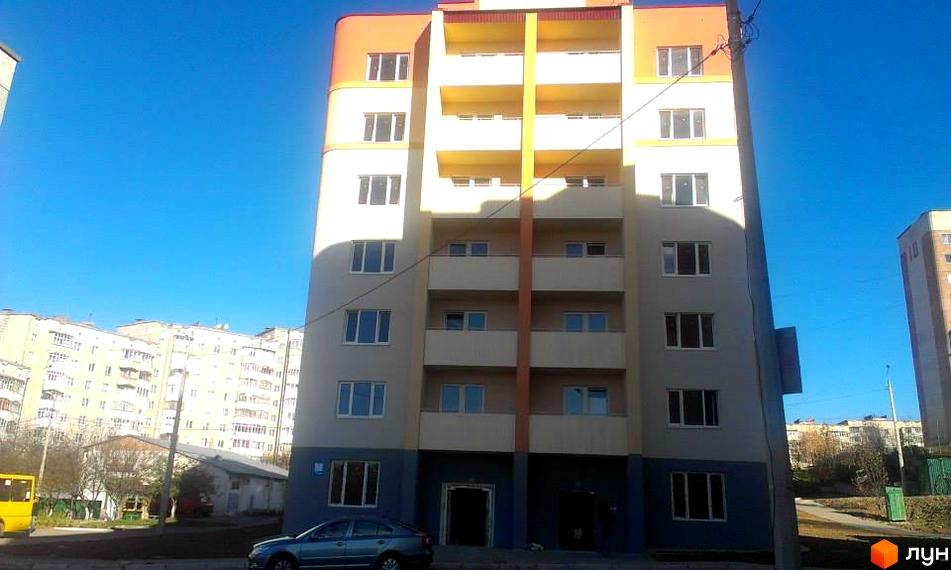 Житловий комплекс Родинний: багатоповерховий будинок з бежевим фасадом, помаранчевими та жовтими балконами, темно-сірим цоколем. Поруч дорога та дерева.