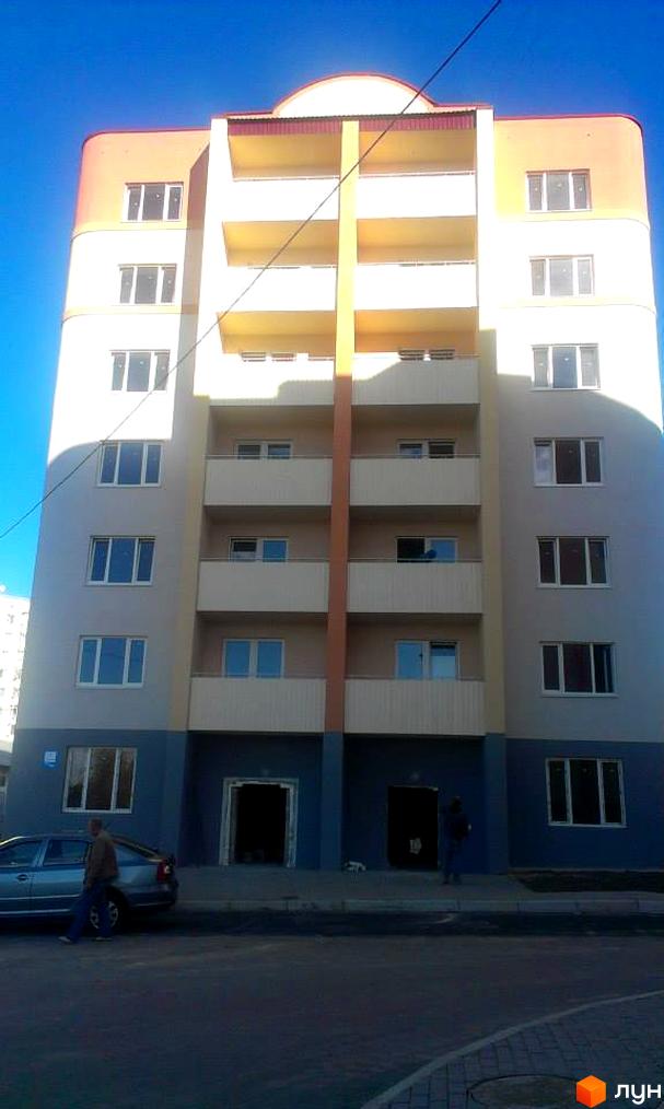 Житловий комплекс Родинний: багатоповерховий будинок з помаранчевим дахом, світлими фасадами та балконами. Перед будинком дорога та автомобіль.