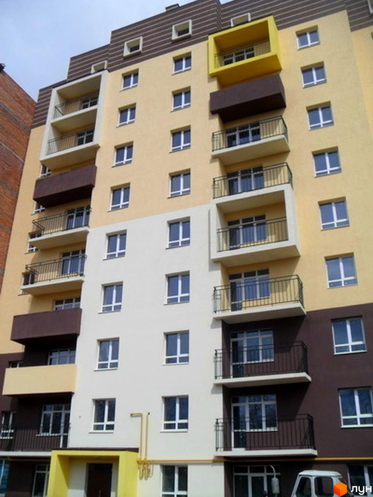 Багатоповерховий будинок Житлового комплексу Родинний затишок з бежевим, білим та коричневим фасадом, балконами та вікнами. Видно жовтий балкон та вхідну групу.