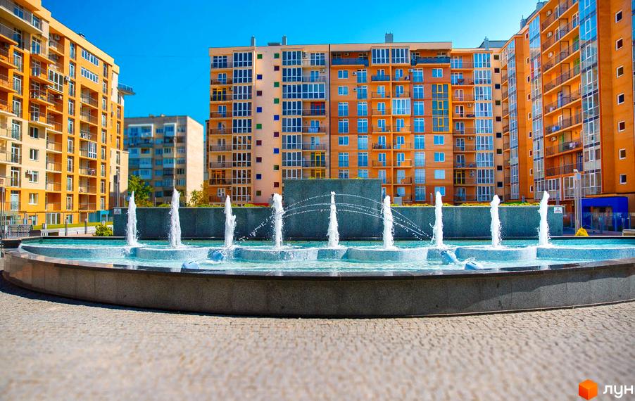 Житловий комплекс Водограй: багатоповерхові житлові будинки з помаранчевими фасадами, великими вікнами та балконами. На передньому плані круглий фонтан.