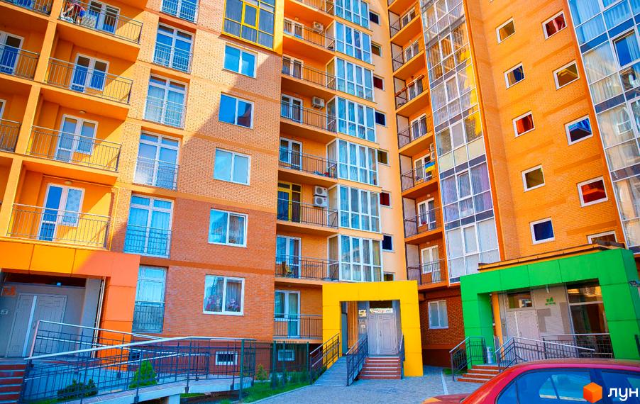 Житловий комплекс Водограй: багатоповерховий будинок з помаранчевим фасадом, балконами та великими вікнами. Вхідні групи з пандусами та доріжками.