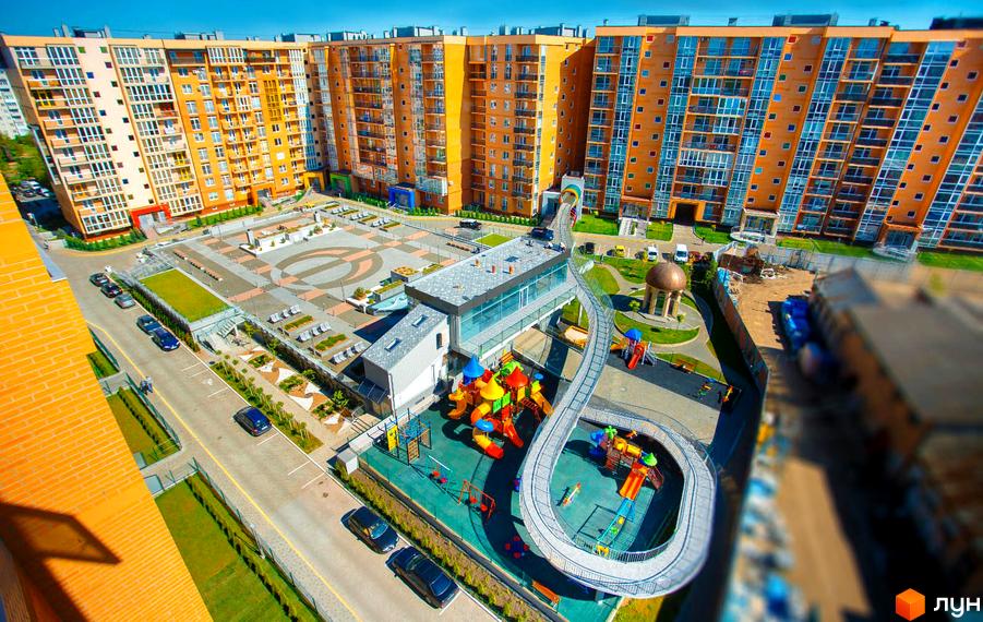 Житловий комплекс Водограй: високі будинки з помаранчевими фасадами та великий внутрішній двір з дитячим майданчиком і пішохідним мостом.