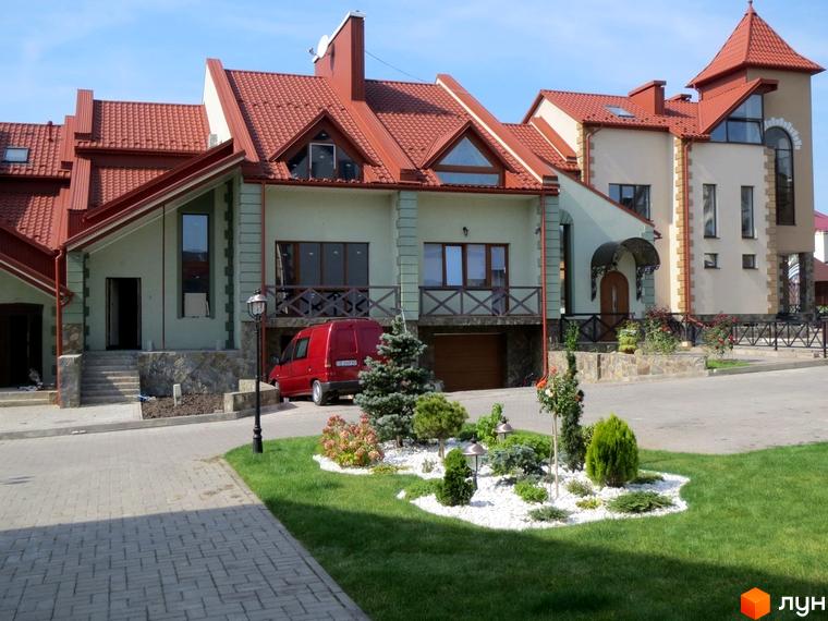 Будинки Котеджного містечка Віденська брама з червоними дахами, світлими фасадами та кам'яними елементами. На передньому плані доглянутий газон та декоративні насадження.