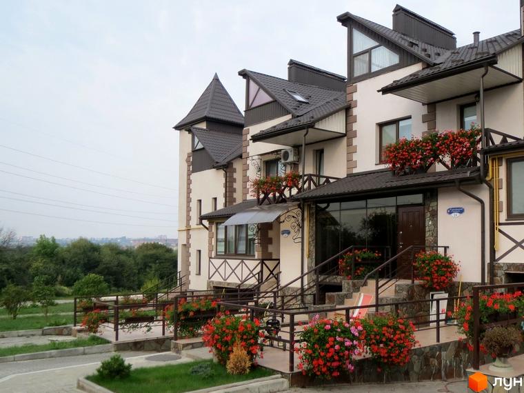 Будинки Котеджного містечка Віденська брама з бежевими фасадами, коричневими дахами та балконами, прикрашеними квітами. Доглянута прибудинкова територія з газонами та доріжками.