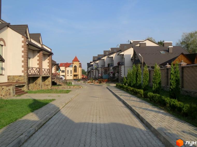 Котеджне містечко Віденська брама: будинки з бежевими фасадами, оздоблені коричневим каменем, та темними дахами. Доглянута вулиця з бруківкою та зеленими насадженнями.