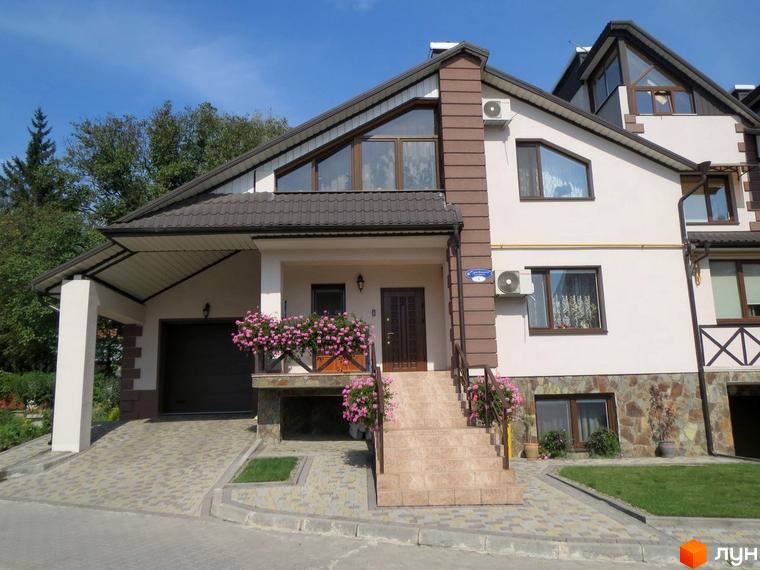 Котеджне містечко Віденська брама: будинок з коричневим дахом, світлими стінами, гаражем та доглянутою прибудинковою територією з квітами.