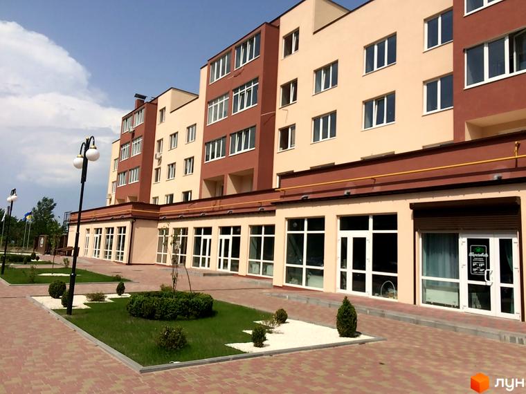 Новобудова ЖК Другий Парковий з фасадом в бежевих та коричневих тонах. Прибудинкова територія з газоном, кущами та бруківкою.