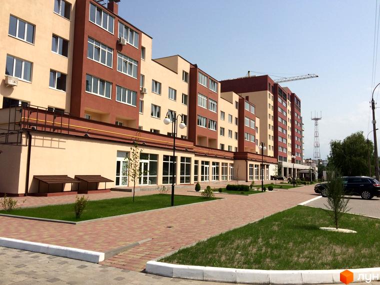 Зовнішній вигляд новобудови ЖК Другий Парковий з коричневими та бежевими фасадами, вікнами та прибудинковою територією з бруківкою та газоном.