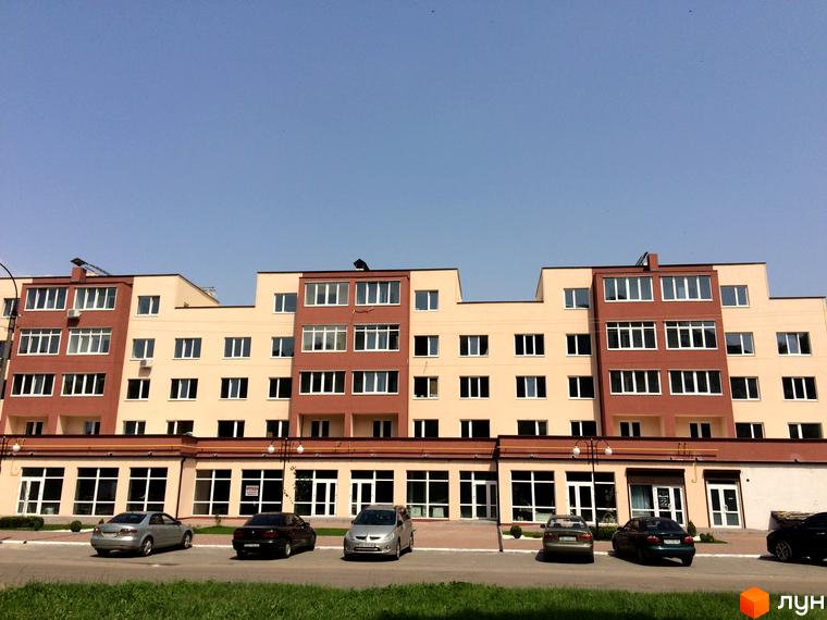 Зовнішній вигляд новобудови ЖК Другий Парковий з коричневими та бежевими фасадами, великою кількістю вікон. Перед будинком розташована парковка з автомобілями та зелена зона.