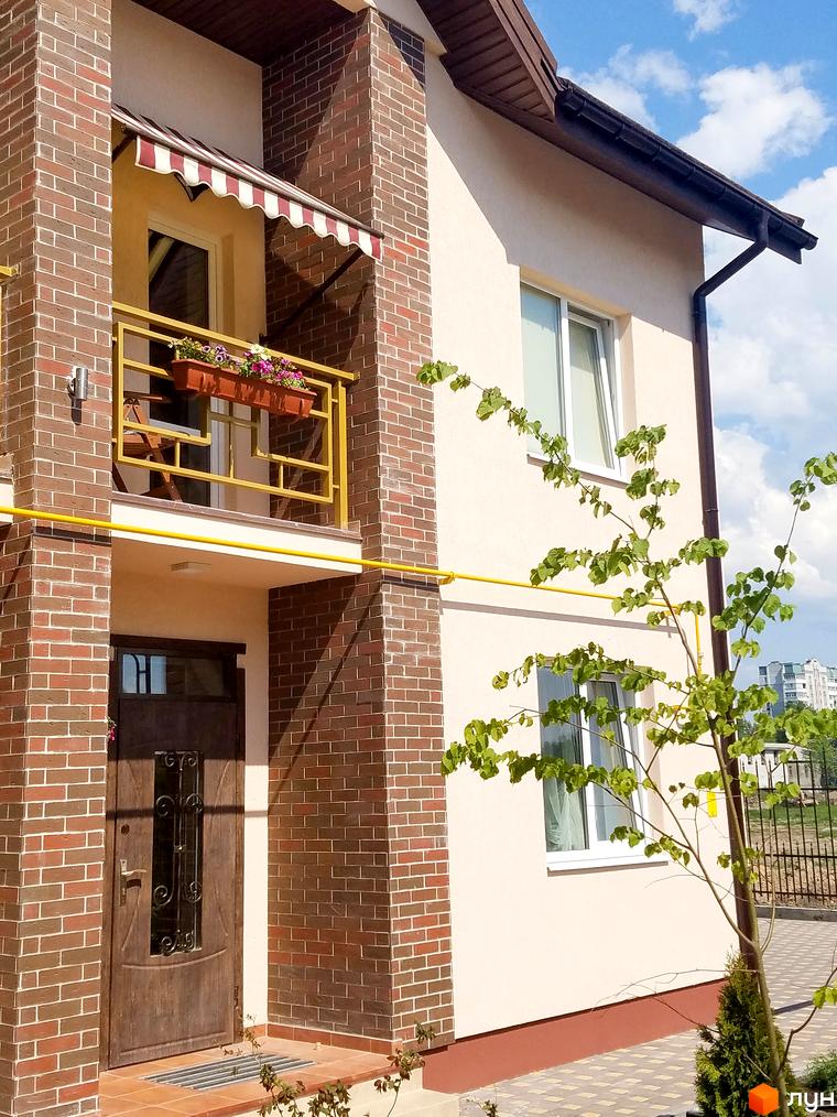 Фасад будинку ЖК Другий Парковий з цегляним оздобленням та балконом з квітами. Прибудинкова територія з деревами та парканом.