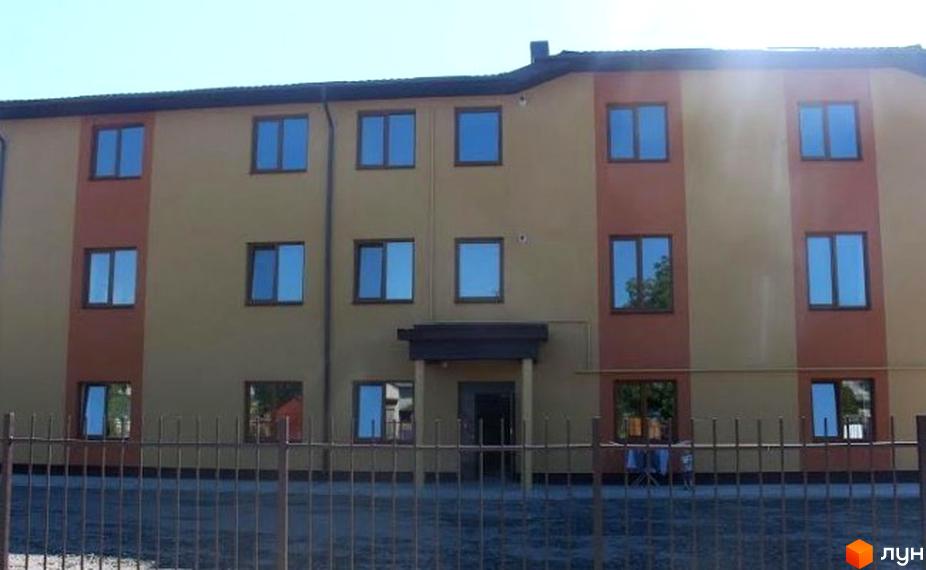 Фасад новобудови на вулиці Ціолковського, 17, з двома кольорами стін та великою кількістю вікон. Перед будинком розташований паркан та зелена зона.