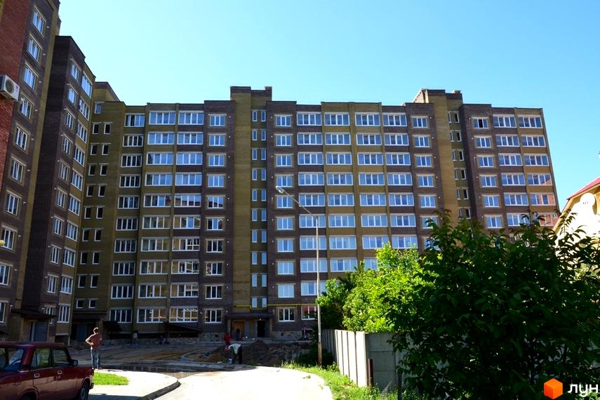 Багатоповерховий житловий комплекс на вул. Іващенка, 1а. Зовнішній вигляд будинку з цегляним облицюванням та численними вікнами. Прибудинкова територія з дорогою та зеленими насадженнями.