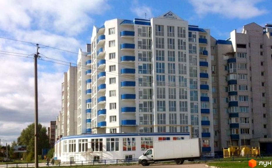 Новобудова на вул. 1-ої танкової бригади (Бєлова), 29. Багатоповерховий будинок білого кольору з синіми балконами та великою кількістю вікон. На передньому плані видно частину прибудинкової території та білу вантажівку.