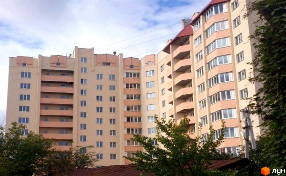 Зовнішній вигляд багатоповерхового житлового комплексу на вул. Зелена, 10. Будинок має світло-бежевий фасад з рожевими елементами та балконами. Навколо будинку зелені насадження.