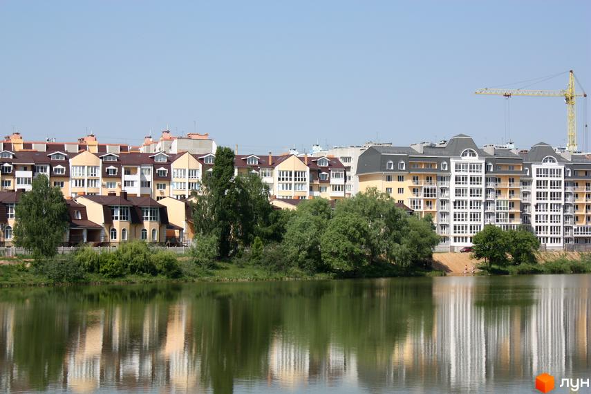 Житловий комплекс Стрелецкая набережная: сучасні багатоповерхові будинки з балконами та панорамними вікнами, розташовані біля озера. На території видно дерева та будівельний кран.