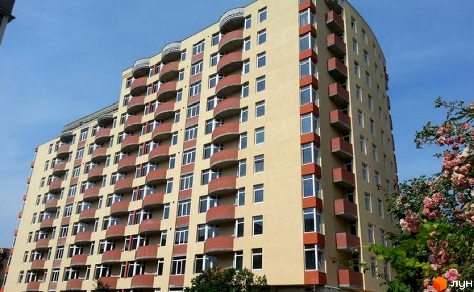 Будівельний проєкт на вул. Володимира Лучаковського, 6а. Багатоповерховий будинок кремового кольору з червоними балконами та великою кількістю вікон. Поруч ростуть дерева з рожевими квітами.