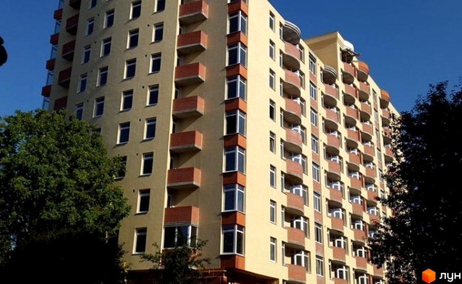 Зовнішній вигляд багатоповерхового житлового комплексу на вул. Володимира Лучаковського, 6а. Будинок має світло-жовтий фасад та червоні цегляні балкони. Навколо будинку зелені дерева.