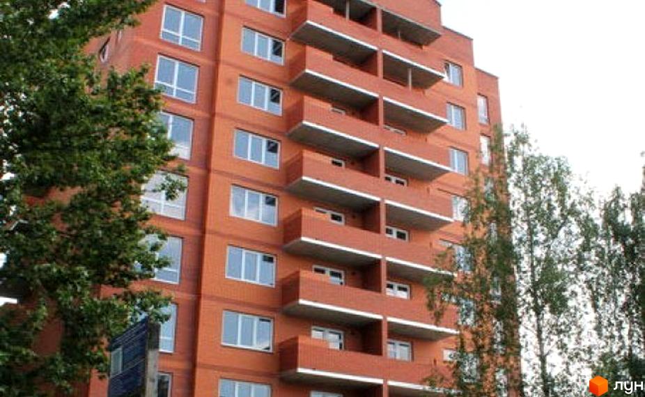 Фасад цегляної новобудови з балконами та вікнами. Навколо будівлі зелені дерева.