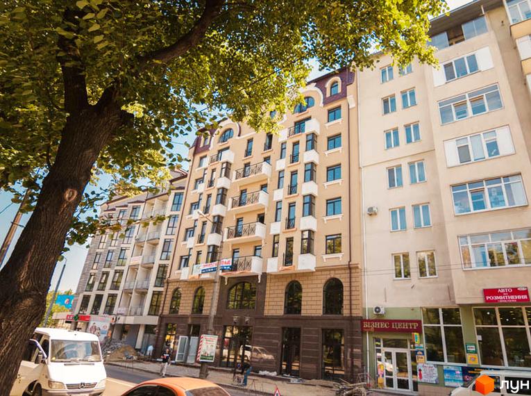 Житловий комплекс Перспектива Хол – фасади будинків з великою кількістю вікон та балконів, розташований біля зеленого дерева. Зовнішній вигляд новобудови.