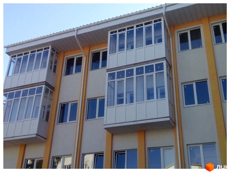 Фасад новобудови на вул. Дмитрівська, 19, з балконами та вікнами. Зовнішній вигляд будівлі з елементами жовтого кольору.
