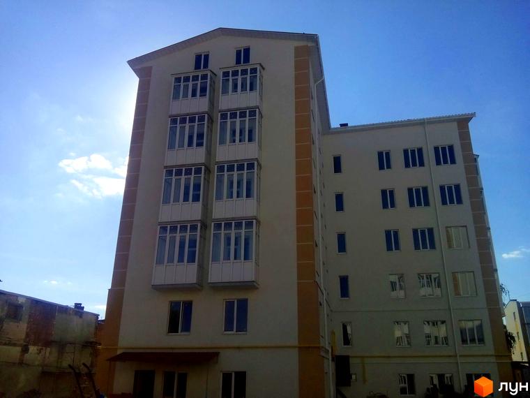 Зовнішній вигляд багатоповерхового будинку з балконами та вікнами на фоні блакитного неба. Новобудова на вул. Дмитрівська, 19.