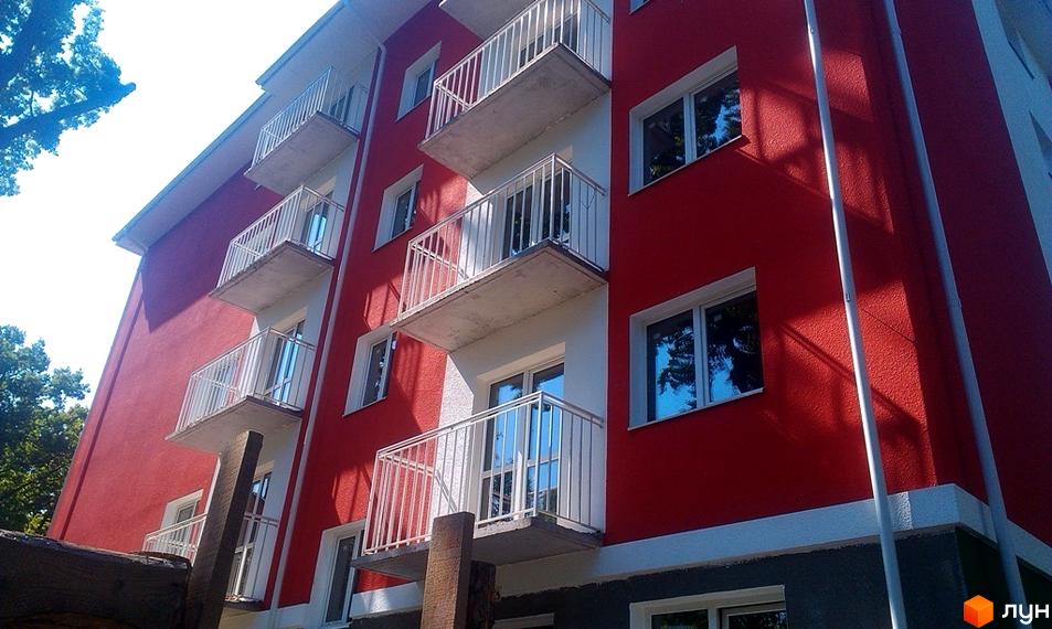 Житловий комплекс Щасливий: яскрава червона фасадна стіна з білими балконами та вікнами. Зовнішній вигляд новобудови.