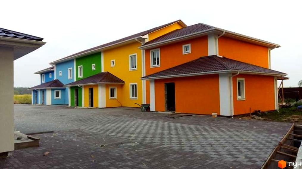 Яскраві таунхауси Ivankiv-townhouse з різнокольоровими фасадами: сині, зелені, жовті та помаранчеві. Навколо будівель облаштований бруківкою двір.