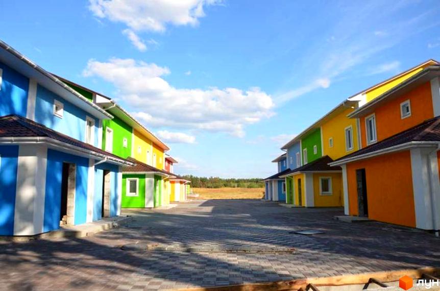 Яскраві таунхауси Ivankiv-townhouse з різнокольоровими фасадами, розташовані на брукованій території під блакитним небом. Комплекс має привабливий зовнішній вигляд.