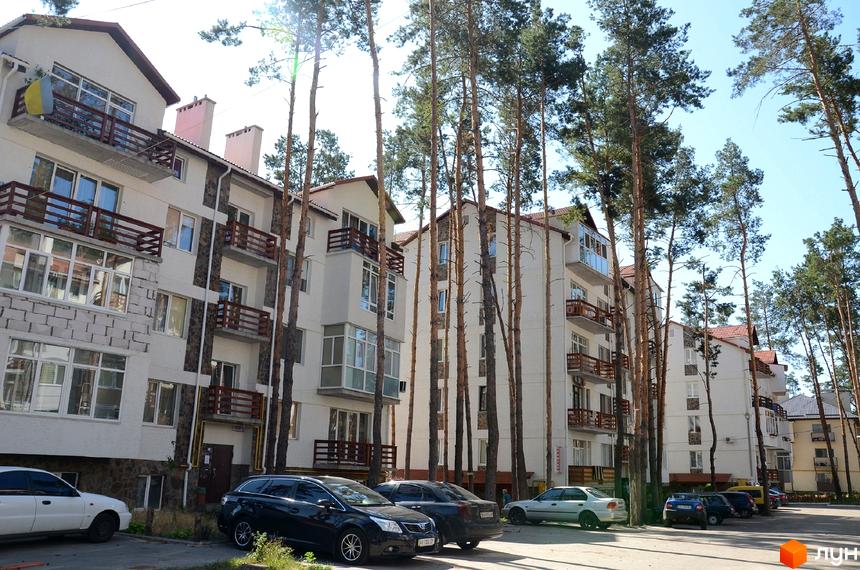 Зовнішній вигляд житлового комплексу Островський з балконами та вікнами. Навколо будівель ростуть високі дерева. Біля будинку припарковані автомобілі.