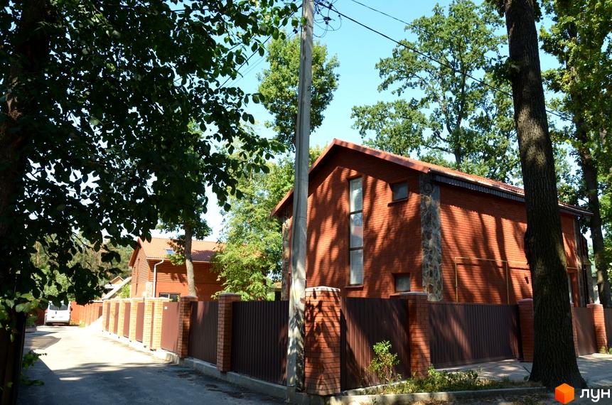 Будинок з червоної цегли з кам'яними вставками та коричневим парканом на вулиці Давидчука. Навколо будинку зелені дерева та сонячне небо.