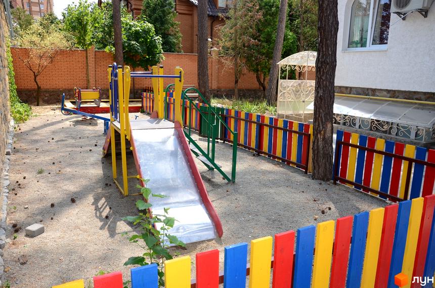 Дитячий майданчик з гіркою та гойдалкою біля будинку ЖК Затишний на вулиці Університетській. Яскрава огорожа розділяє територію комплексу.