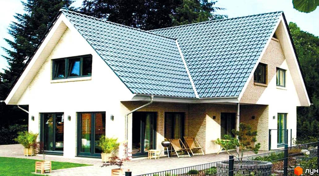 Котеджне містечко Родзинка: двоповерховий будинок з черепичним дахом, великими вікнами та терасою. Навколо будинку доглянутий двір з газоном та рослинами.