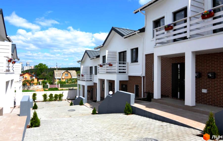 Зовнішній вигляд таунхаусів Сервус з білими фасадами та цегляними елементами. Прибудинкова територія з бруківкою та зеленими насадженнями.