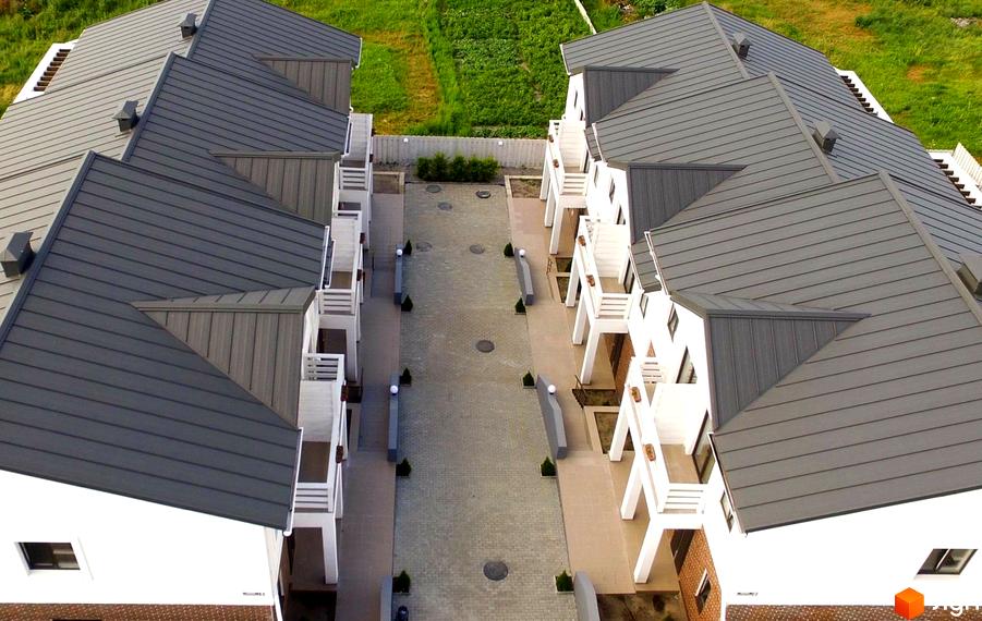 Таунхауси Сервус з сірими дахами та білими фасадами, розташовані вздовж вимощеного внутрішнього подвір'я з зеленими насадженнями.