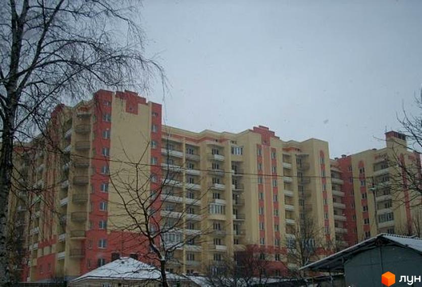 Житловий комплекс Західні ворота з фасадом у світлих тонах та червоними елементами. Прибудинкова територія з деревами та невеликими будівлями.