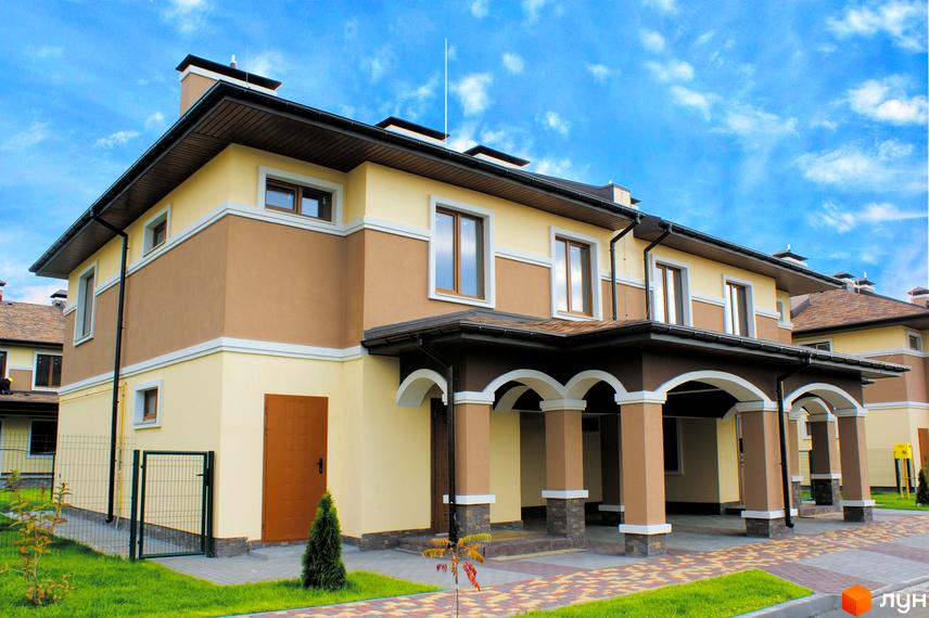 Еко-поліс Оксамит - сучасний житловий комплекс з двоповерховими будинками, оздобленими світлою штукатуркою та коричневими акцентами. Територія навколо будівель доглянута, з газонами та бруківкою.