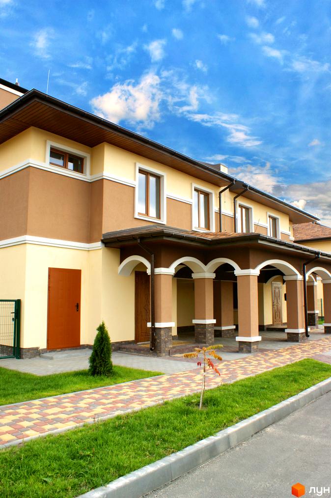 Еко-поліс Оксамит: двоповерхові будинки з коричневою та світло-жовтою штукатуркою, аркадою та бруківкою. Навколо будівель зелена газонна трава та доглянута територія.