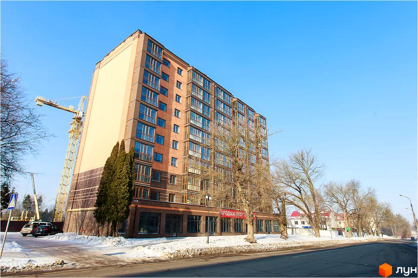 Зовнішній вигляд багатоповерхового будинку ЖК Сімейний з цегляним фасадом та великими вікнами. Навколо будівлі видно дерева та засніжену територію.