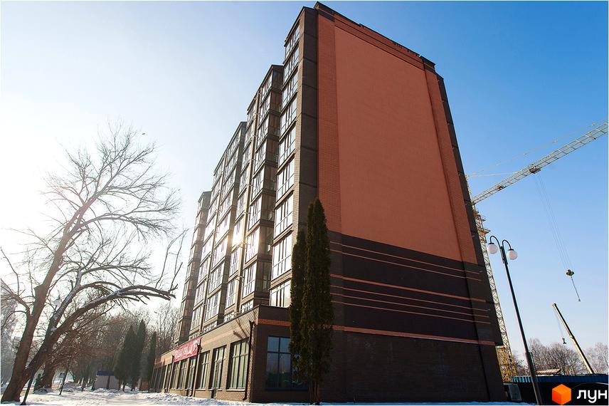 Житловий комплекс Сімейний – це багатоповерхова новобудова з цегляним фасадом та численними вікнами. Навколо будівлі видно дерева та будівельний кран.