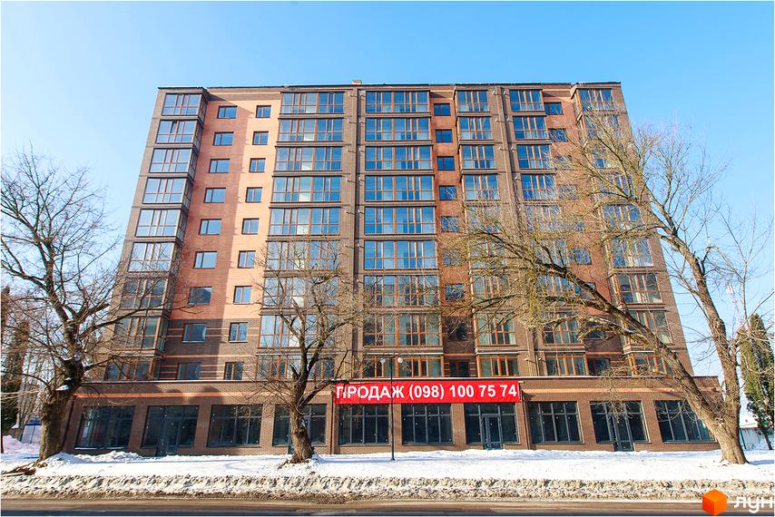 Фасад цегляної новобудови ЖК Сімейний з численними вікнами та балконами. Перед будинком видно дерева та засніжену територію.