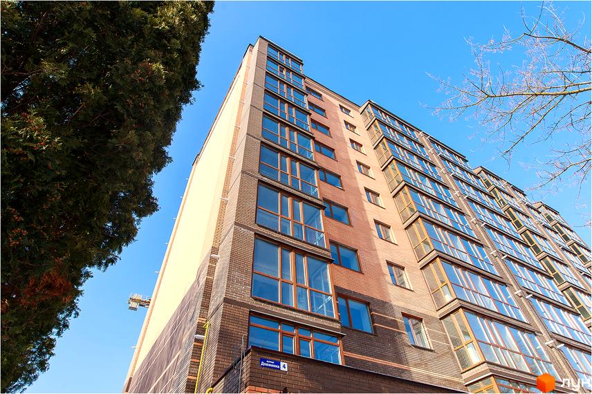 Зовнішній вигляд новобудови ЖК Сімейний з цегляним фасадом та великими вікнами. Будинок розташований на фоні блакитного неба з деревами.