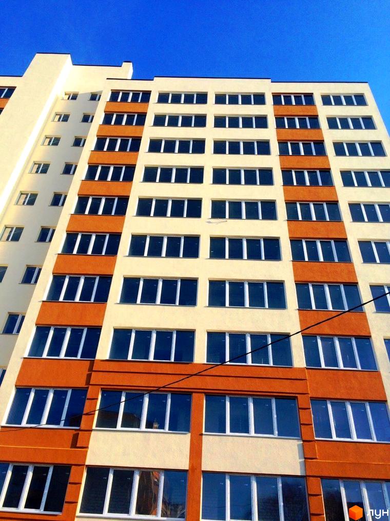 Зовнішній вигляд житлового комплексу Затишна Оселя. Багатоповерховий будинок з вікнами та балконами на тлі блакитного неба.