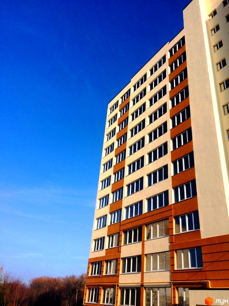 Фасад житлового комплексу Затишна Оселя з коричневими та бежевими елементами під яскраво-синім небом. Вікна розташовані рядами на поверхах будівлі.